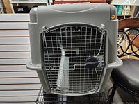 Front view of large grey plastic pet carrier kennel with metal wire door and locking handle visible.