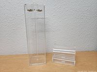 Photo showing front view of two clear acrylic jewelry cases on white background: one tall with dual earring rods, one smaller tiered case.