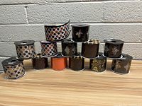 Full view of 15 assorted rolls of Halloween ribbons stacked in pyramid formation on table against cinderblock wall, featuring various designs including polka dots, ghosts, skulls, and metallic accents.