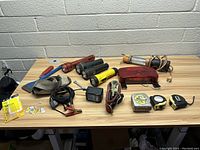 Lot of assorted tools and flashlights laid out on a wooden table including flashlights, clamps, tape measures, straps, and various hand tools.