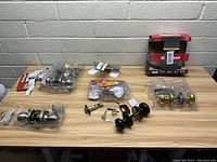 Photo of multiple door locks including knob locks, lever handles, deadbolt parts, mounting hardware, some in packaging, others loose with keys.
