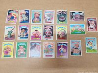 Top-down view of 20 different Garbage Pail Kids trading cards arranged in rows on a flat surface.