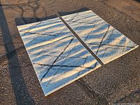 Two matching rectangular rugs laid flat outdoors, showing the abstract intersecting dark lines on light background.