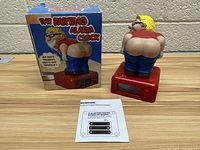 The Farting Alarm Clock shown with its original colorful box and instruction sheet on a wooden surface.