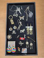 Tray of assorted jewelry including earrings, pins, necklaces, and keychains displayed on black felt background