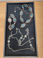 Tray showing two silver-tone belts with turquoise stones and two silver chains with floral motifs laid flat.