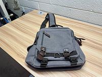 Front side view of the gray one strap canvas carrying bag with buckle details, zippered compartments, and adjustable strap.