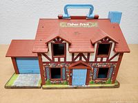 Front view of the vintage Fisher Price Tudor House playset showing detailed painted facade, blue door, and garage extension.