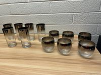 Set of 12 vintage drinking glasses displayed with silver rims, including 6 tall ones and 6 short rounded ones