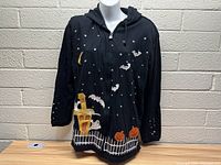 Full front view of the black zip-up hoodie with Halloween decorations including bats, stars, pumpkins, ghosts, a crescent moon, and a haunted house.