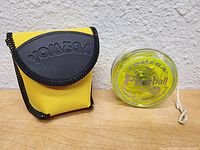 Yellow and black Yomega branded carrying case and Yomega Fireball yo-yo side by side on a textured wall background.