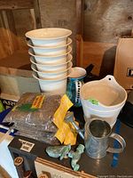 Collection of white garden planters, bags of Spanish moss, metal bird garden faucet and watering pourers on wooden shelves