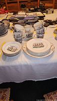 Full view of the china set arranged on a table covered with a white cloth, showing multiple cups stacked, plates laid out, and additional items around