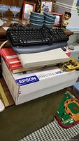 Stack of electronic items including the Epson printer box and multiple keyboards
