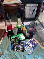 Two lava lamps with red and green lava on bases, multiple handheld electronic games including Battleship, WCW Hulk Hogan, Grand Slam Baseball, and others.