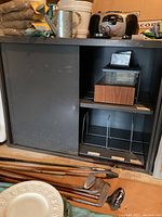 Metal cabinet with sliding door partially open, showing interior shelving with various small boxes stored inside, corner view
