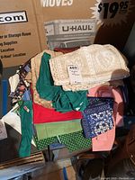 Image of folded assorted table napkins and a beige lace table runner on top of a cardboard box.