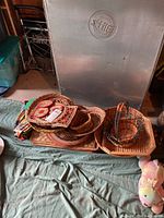 Wide view of multiple wicker baskets stacked, with textile place mats and pot holders on and near them on blue cloth surface.