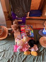 Table display of plush toys including Minnie Mouse, tie-dye and brown bears, puzzles and board games on a green cloth surface.
