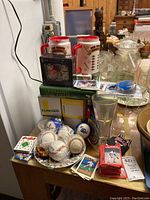 Photo showing baseball cards, two white and red Yankees beer mugs, several baseballs and softballs on a plate, the book 'Leveling the Field', and other sports memorabilia items on a table.