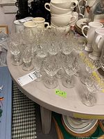 Photo showing multiple rows of clear etched glass stemware arranged on a round table with other ceramic dishes and cups in the background.