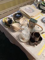 Photo of various ceramic and glass teacups, mugs, teapot, and serving dishes on a table with a price tag