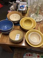 Overview of the assortment of large bowls in yellow, blue, beige, and brown colors with some nested inside one another on a wood table.