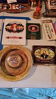 Lot of vintage tins and two gold-toned ashtrays displayed on a table with various colorful vintage tin designs and printed portraits.