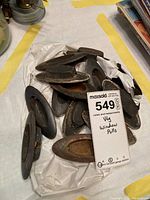 Metal window pulls piled on a white surface with a tag marked '549' and 'window pulls'. Mostly oval-shaped, showing rust and patina indicating age and wear.