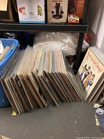 Photo showing rows of vinyl records stored under a shelf with protective sleeves and album covers visible.