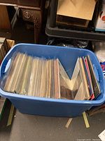 Blue plastic bin filled with a large number (approx 50) of vinyl record albums, mostly in plastic sleeves.