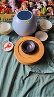 Photo showing 6 wood plates stacked, 1 round wood serving bowl, 9-inch round blue vase, assorted ceramic bowls, and 2 spoon holders with red lobster design.