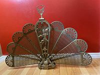 Front view of the brass peacock folding fireplace screen showing fan-shaped panels and central figure.