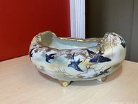 Side view of oval footed porcelain bowl with hand painted flying birds and gold accents on branches.
