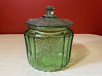 Front view of green glass biscuit jar with lid showing embossed floral pattern and ribbed vertical panels