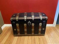 Front view of black metal trunk with wood slats and brass ornaments