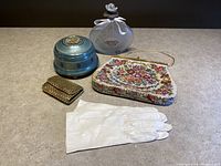 Image showing all four items: white Italian leather gloves, floral needlepoint handbag, blue metal powder music box, and gold-tone key holder wallet.