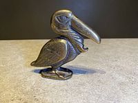 Side view of solid brass pelican bottle opener showing detailed carving on wings and beak.
