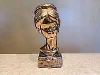Front view of ceramic woman's bust with bronze glaze on neutral background.