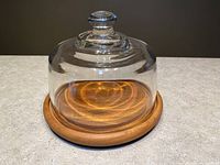 Front view of the glass cloche on teak wooden base, showing clear dome and smooth wood base.