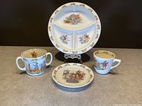 Photo of Royal Doulton Bunnykins divided plate, tea cup and saucer, and two additional collectible Bunnykins cups.
