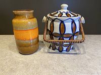 Two items side by side on neutral surface: left is a Scheurich banded glaze vase in orange, brown, green tones; right is an Erphila covered jar with geometric pattern and cane-style handle.
