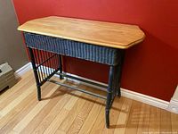 Front and side view of vintage bamboo desk with wood top and green wicker base on hardwood flooring against red wall.