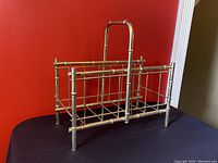 Front and side view of vintage brass bamboo magazine rack on black table against red background