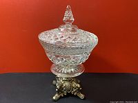 Full view of the vintage crystal candy dish with lid and brass eagle base, showing the intricate cut-glass pattern and finial on lid.