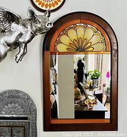 Mirror hanging on wall next to wall decor showing reflective surface and stained glass arch design.