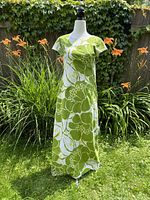 Front view of the vintage Hawaiian dress displayed on a mannequin outdoors. Green and white floral pattern visible with short sleeves and ankle length.
