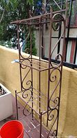 Full view of the painted metal bakers rack displayed outdoors showing ornate scrollwork and condition of paint with chips and scratches.