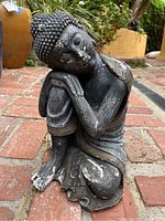 Close-up photo of the black resin Buddha figurine sitting on brick ground with weathering and chipped paint visible.