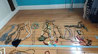Overview of various necklaces and bracelets arranged on wood floor, showing a variety of costume jewelry made of metal and semi-precious stones and beads.